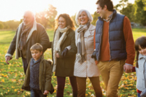 A large multi-generational family walking hand-in-hand through a park. A grandmother and grandfather, mother and father, and a young boy and young girl.